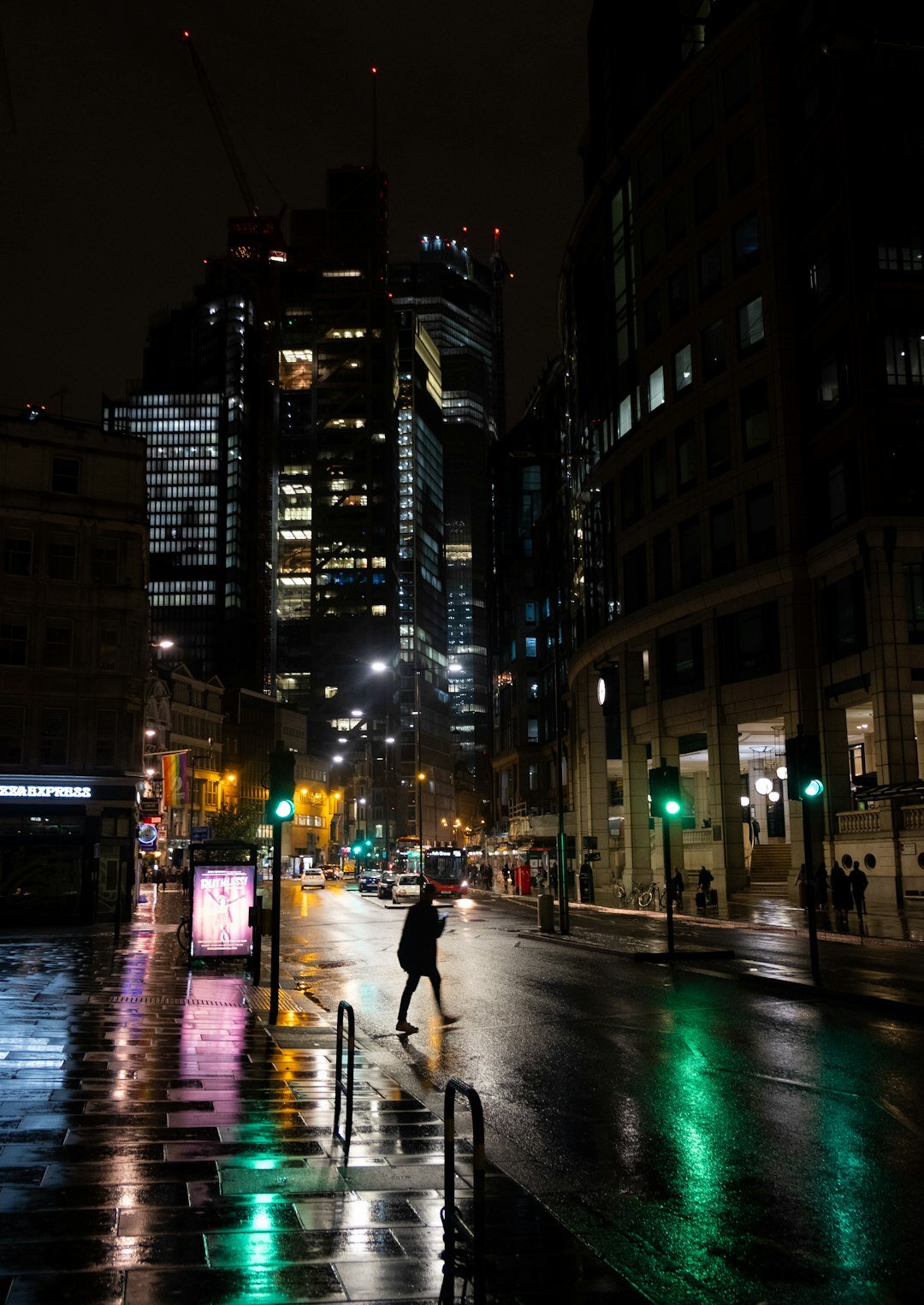 Rainy city street at night with a lone silhouette walking under streetlights
